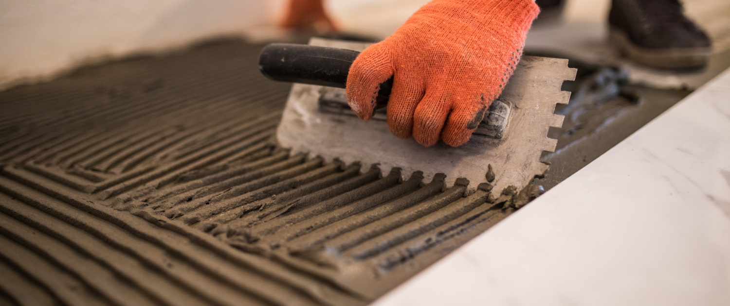 Laying Ceramic Tiles. Troweling mortar onto a concrete floor in preparation for laying white floor tile.